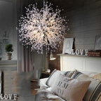 This Clérachic chandelier hangs lit above a rustic bedroom corner with a chest of drawers and a potted plant.