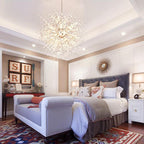 This Clérachic chandelier hangs above a soft bedroom with a tufted headboard and a patterned rug.