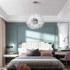 This Clérachic chandelier hangs lit in a teal-walled bedroom with a tufted headboard and a pink cushion.