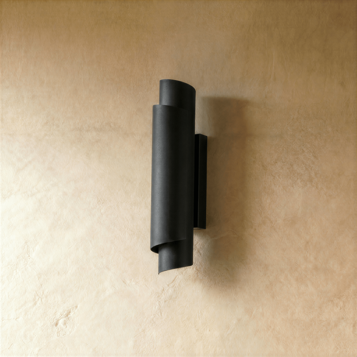 Clérachic wall sconce in matte black, the curled metal form mounted on a pale wall with light spilling up and down.