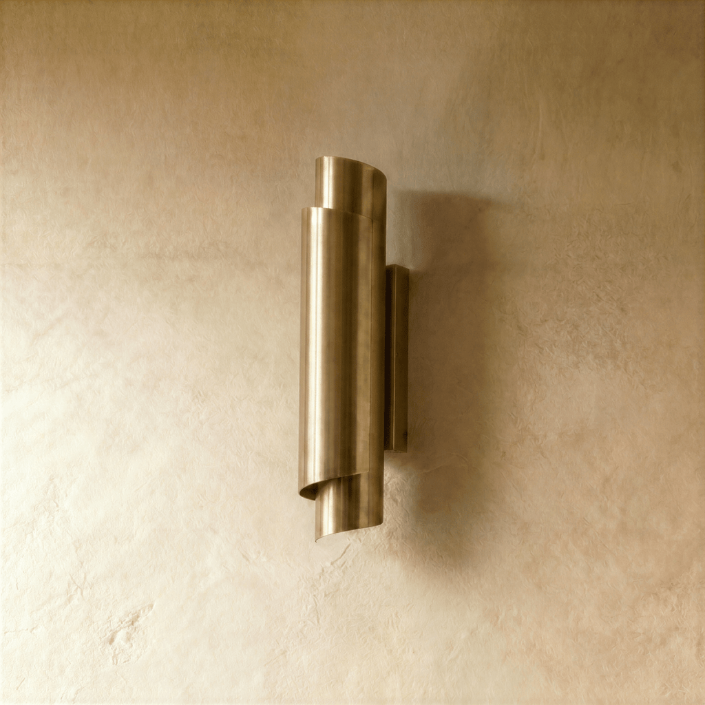 Clérachic wall sconce in polished brass, the curled metal shade set against a plaster wall with light above and below.