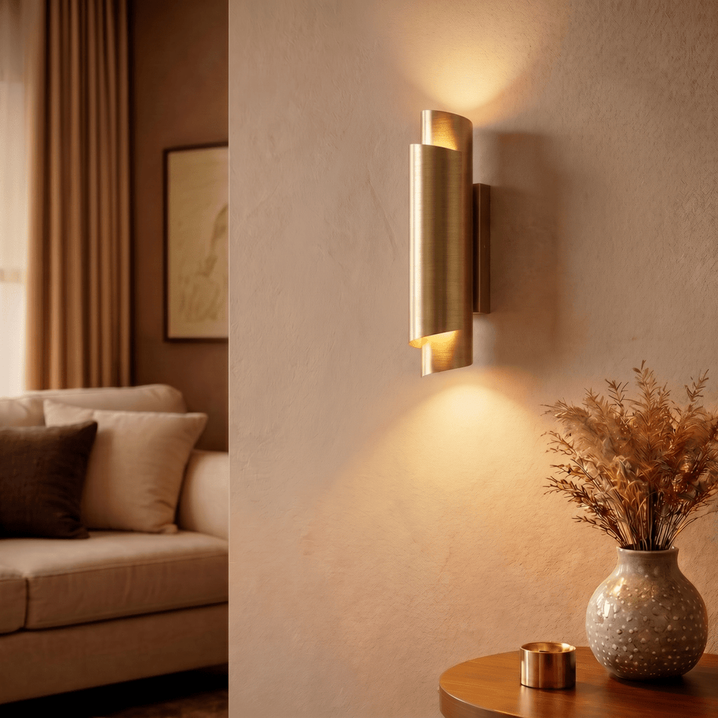 Clérachic brass wall sconce lit above a round side table with a patterned vase and dried grasses in a living room.