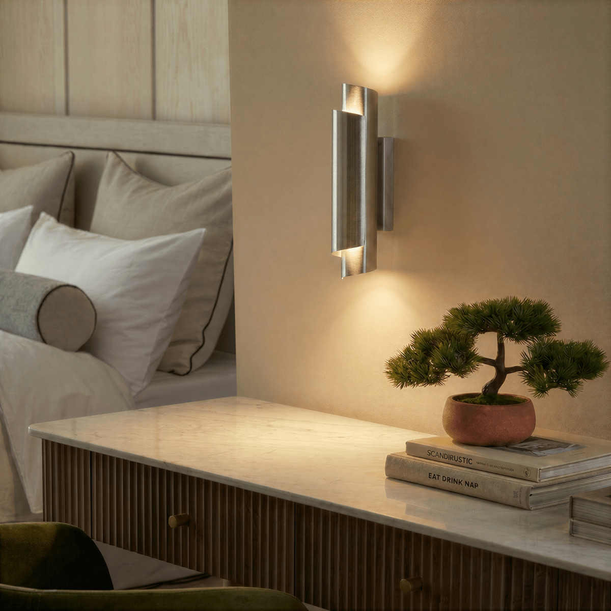 Clérachic chrome wall sconce mounted above a marble nightstand with a bonsai tree and stacked books in a bedroom.