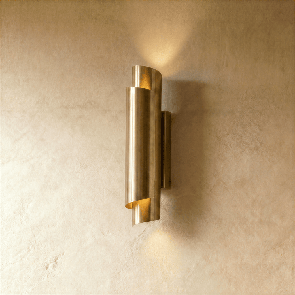 Clérachic wall sconce in a bright brass finish, the rolled cylinder shade throwing light up and down a pale wall.