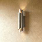 Clérachic wall sconce in a bright chrome finish, the rolled cylinder shade lit softly against a plaster wall.