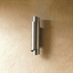 Clérachic wall sconce in chrome, its curled metal shade set on a pale wall with light glowing gently up and down.