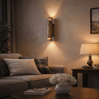 Clérachic vintage brass wall sconce glowing above a sofa with patterned cushions, beside a table lamp in a living room.