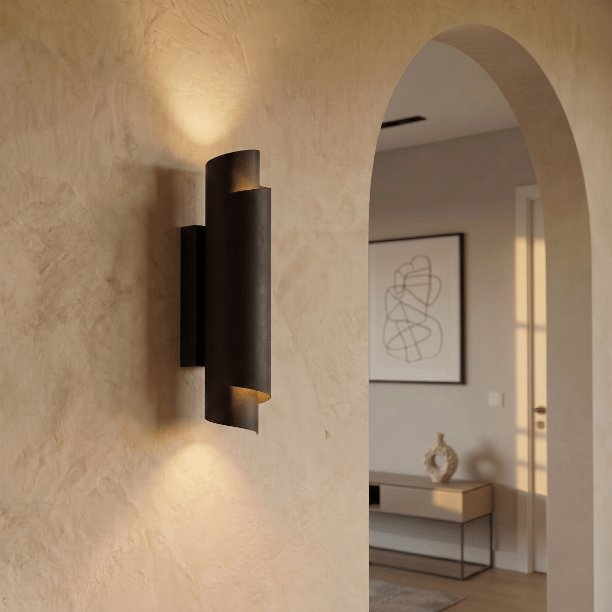Clérachic matte black wall sconce glowing in a plaster hallway beside an archway leading to a sunlit living room.