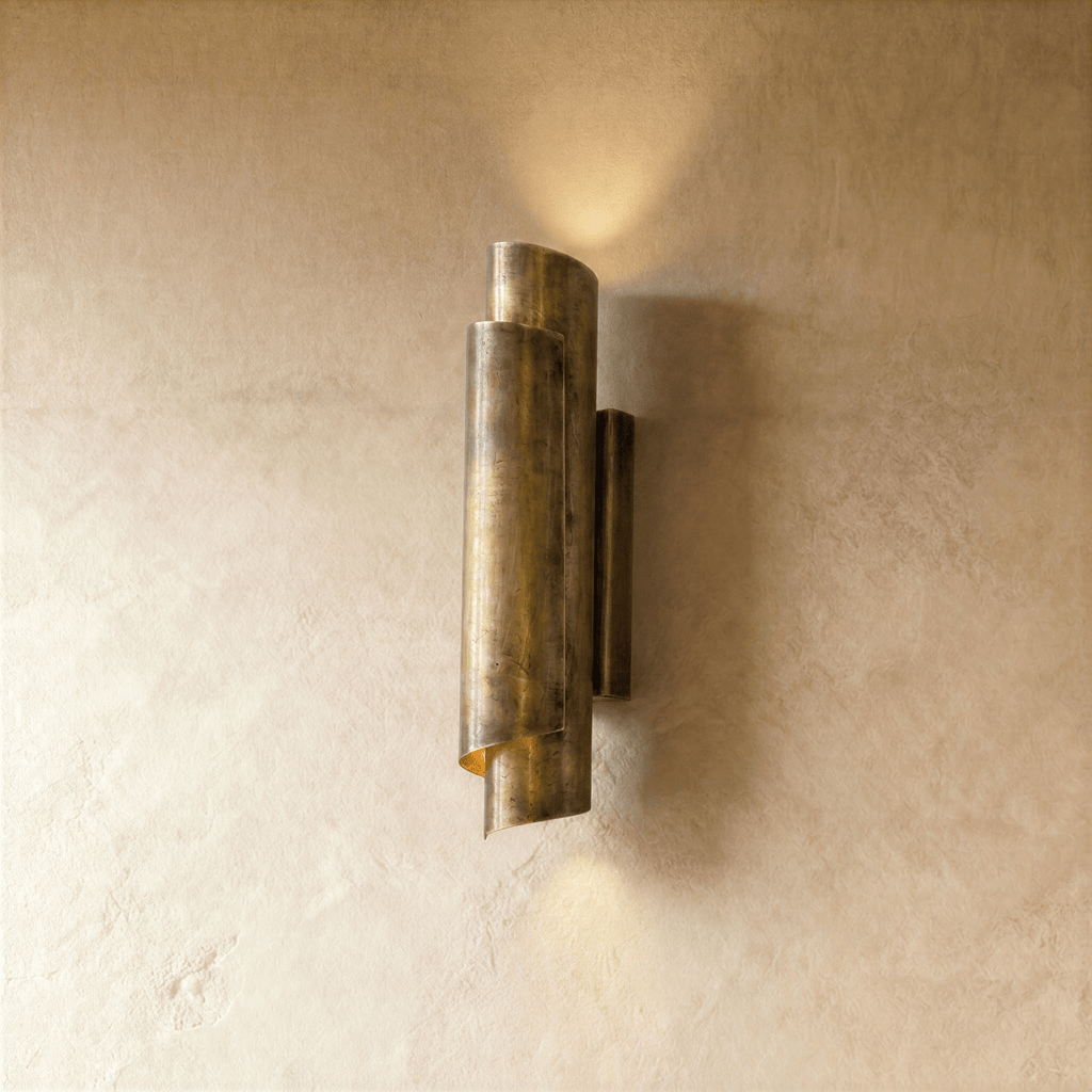 Clérachic wall sconce in vintage brass with a rolled cylinder shade, casting light up and down a plaster wall.