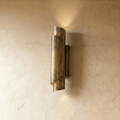 Clérachic wall sconce in vintage brass with a rolled cylinder shade, casting light up and down a plaster wall.