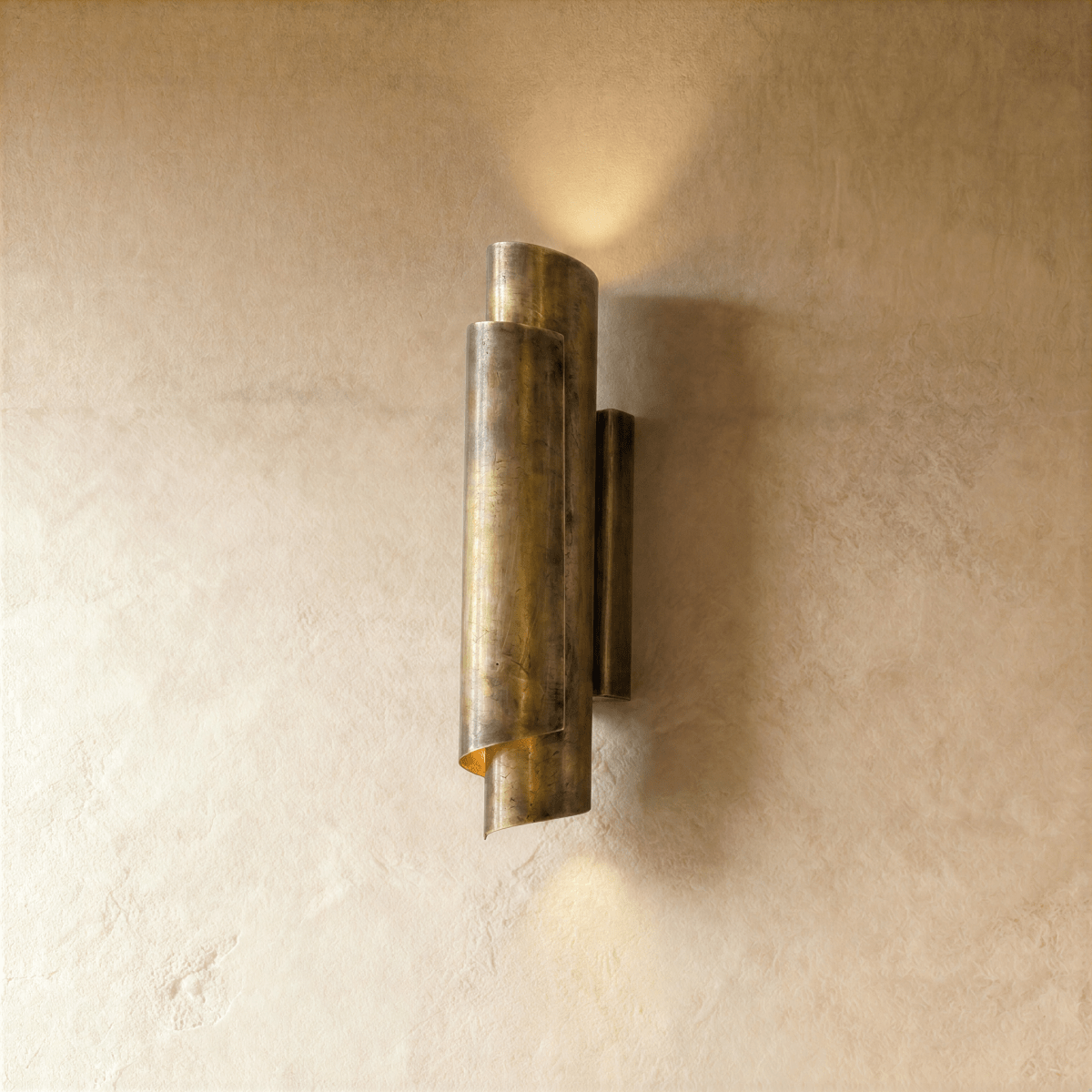 Clérachic wall sconce in vintage brass with a rolled cylinder shade, casting light up and down a plaster wall.