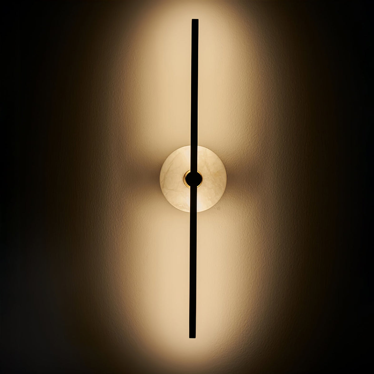 Clérachic wall sconce switched on against a dark background, warm light glowing from behind its alabaster disc.