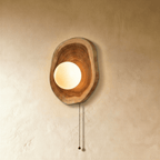 Clérachic wood wall lamp with a frosted glass globe glowing warm white, its beaded pull-chain hanging against a plain wall.