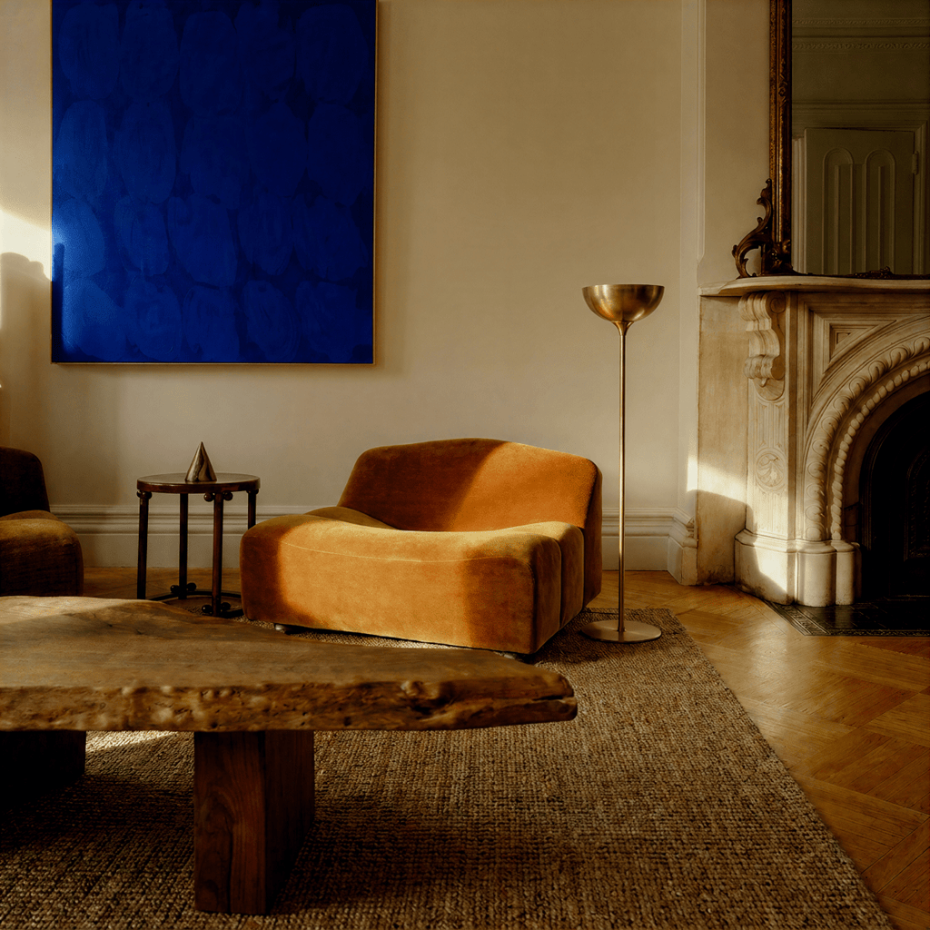 Clérachic vintage brass floor lamp glowing beside an orange sofa and a marble fireplace beneath a dark blue painting.