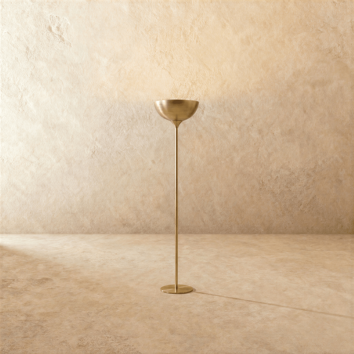 Clérachic floor lamp in a brighter brass finish, its uplight bowl set on a slender stem against a plaster wall.