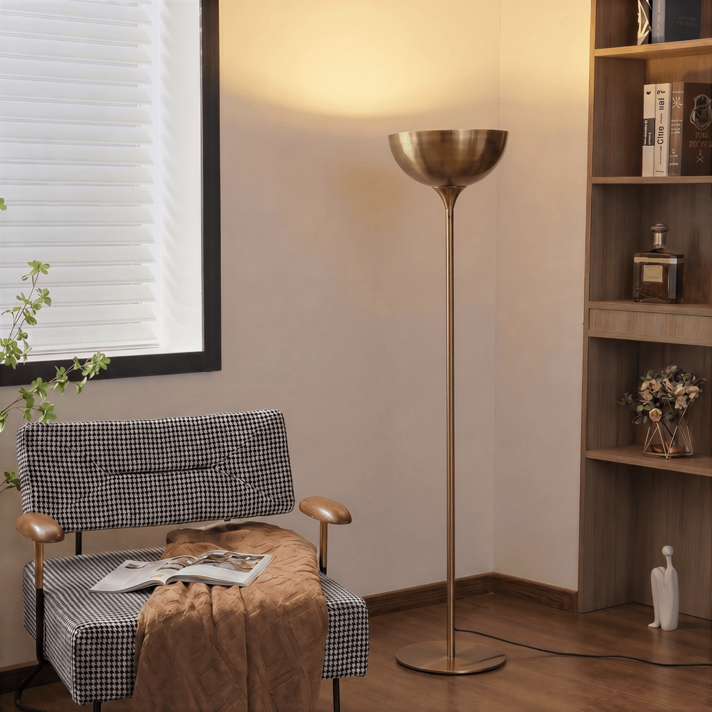 Clérachic vintage brass floor lamp glowing beside a checked armchair and a wooden bookshelf in a reading corner.