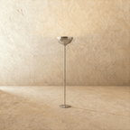 Clérachic floor lamp in a bright chrome finish, its uplight bowl set on a slender stem against a plaster wall.