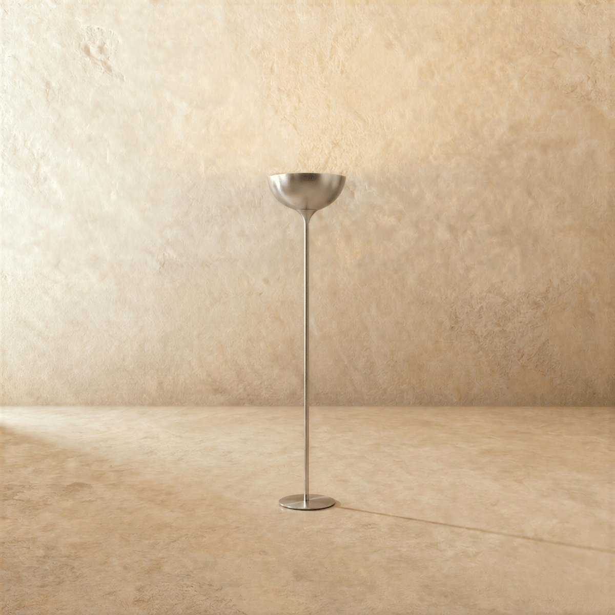 Clérachic floor lamp in a bright chrome finish, its uplight bowl set on a slender stem against a plaster wall.