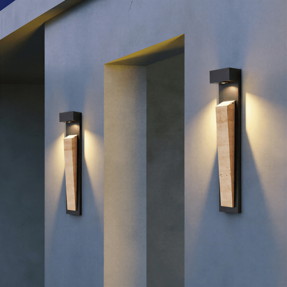 Clérachic wall lamp mounted as a matching pair either side of a recessed doorway, each throwing a wide warm pool across the pale facade at dusk.