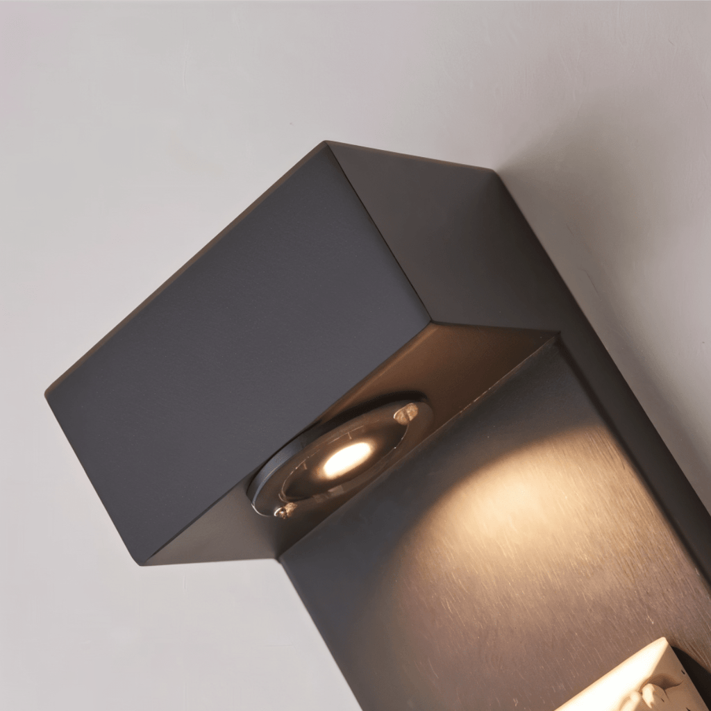 Clérachic wall lamp close-up of the canopy's clear lens, clipped into an angled facet at its lower front corner and aimed down toward the travertine.