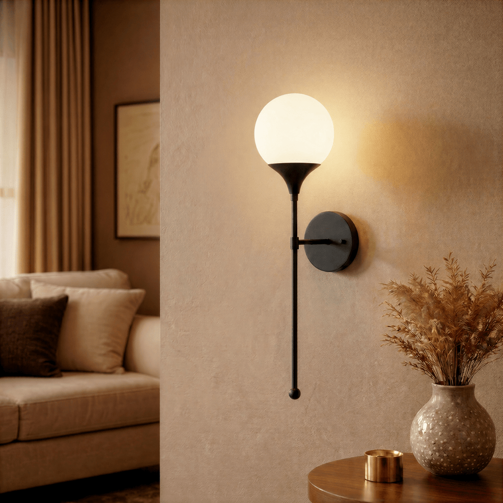 Clérachic wall lamp in matte black glowing beside a beige sofa and a framed landscape print.