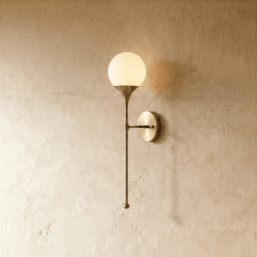 Clérachic wall lamp in a warm satin brass finish, a frosted glass globe glowing on a slender stem.
