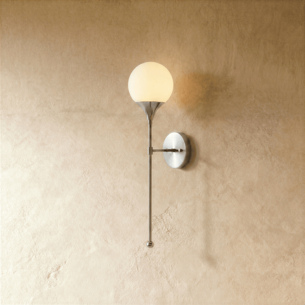 Clérachic wall lamp in chrome, a round frosted glass globe glowing on a slender tapering stem.