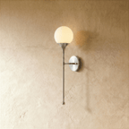 Clérachic wall lamp in chrome, a round frosted glass globe glowing on a slender tapering stem.