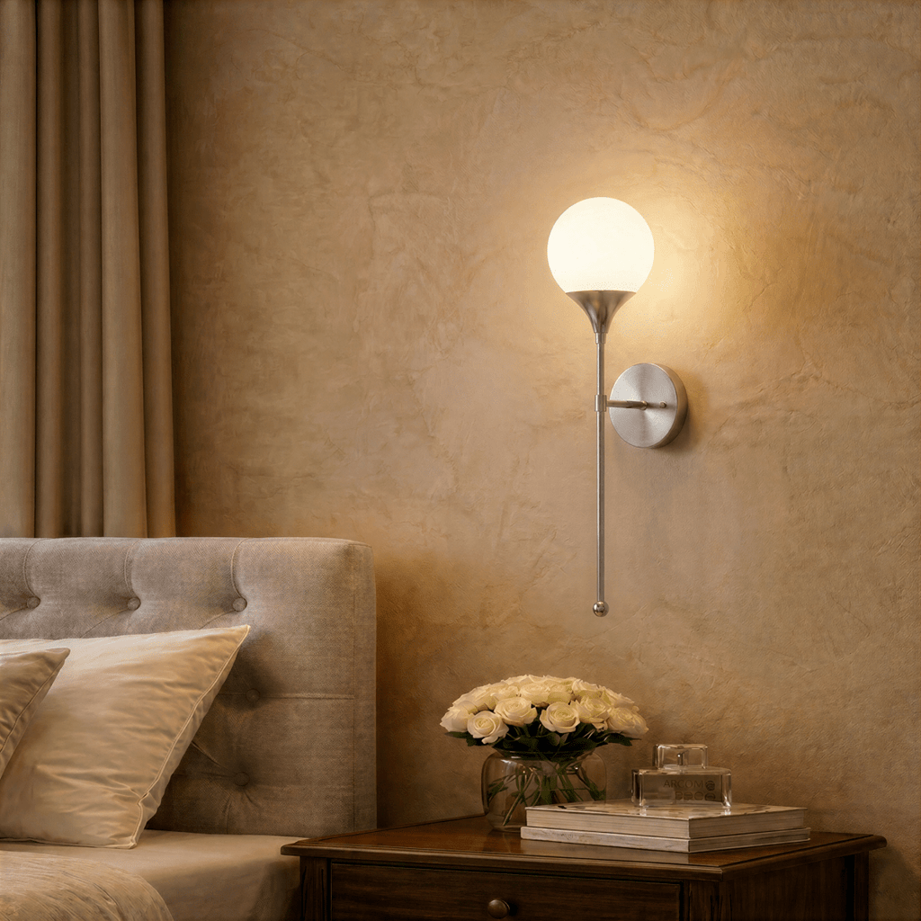 Clérachic wall lamp in chrome lighting a bedroom nightstand set with a vase of white roses.