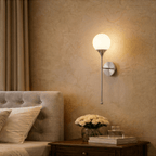 Clérachic wall lamp in chrome lighting a bedroom nightstand set with a vase of white roses.
