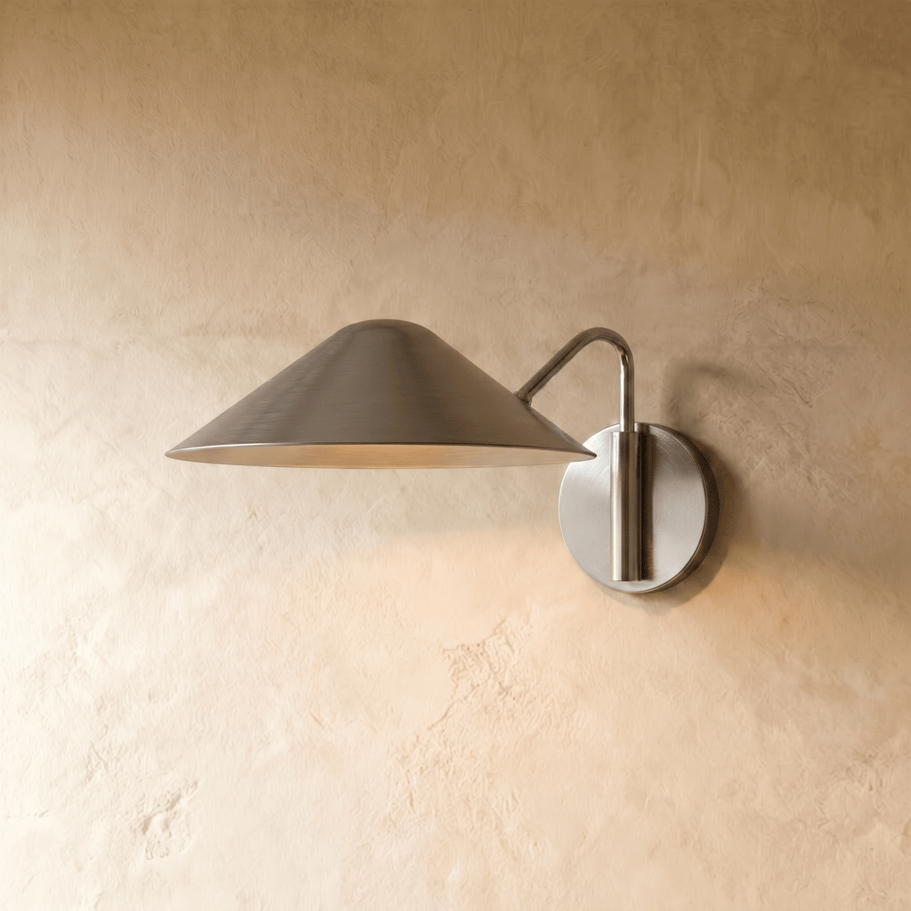 Clérachic cone-shade wall sconce in chrome with a curved arm, mounted on a plaster wall in studio light.