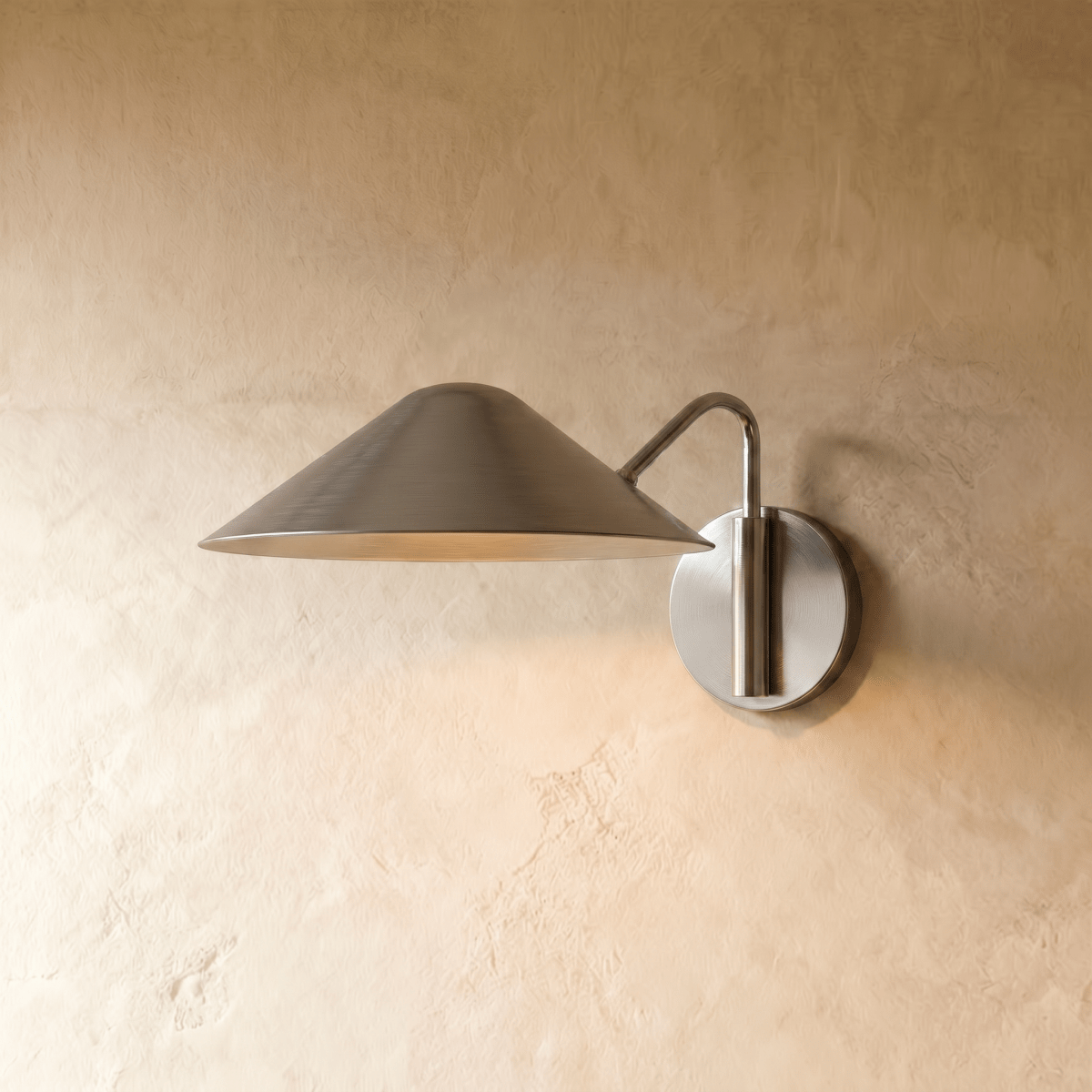 Clérachic cone-shade wall sconce in chrome with a curved arm, mounted on a plaster wall in studio light.