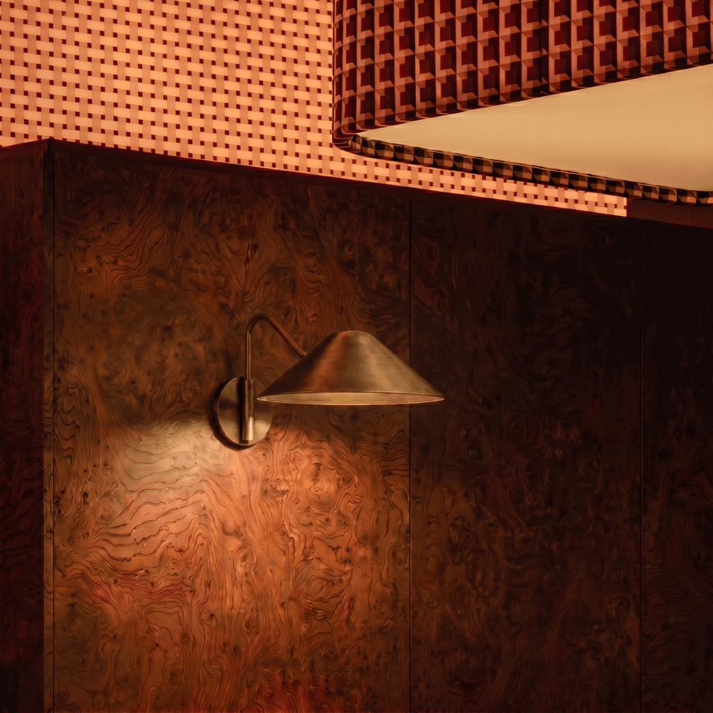 Clérachic vintage brass cone-shade wall sconce lit against a burl-wood panelled wall in a lounge booth.