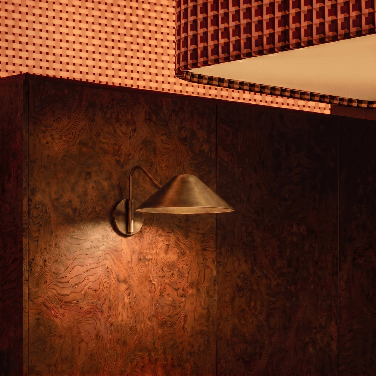 Clérachic vintage brass cone-shade wall sconce lit against a burl-wood panelled wall in a lounge booth.