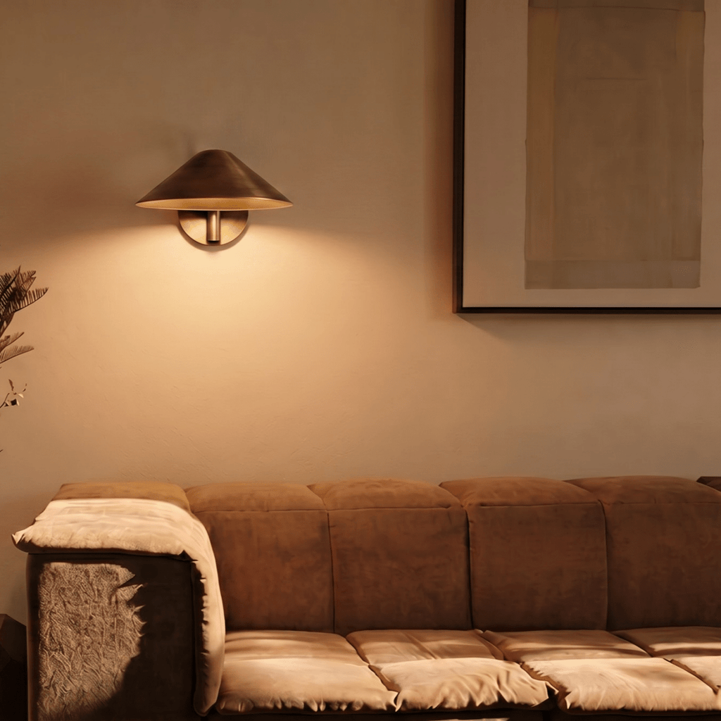 Clérachic vintage brass cone-shade wall sconce lit above a sofa beside a large framed abstract print.