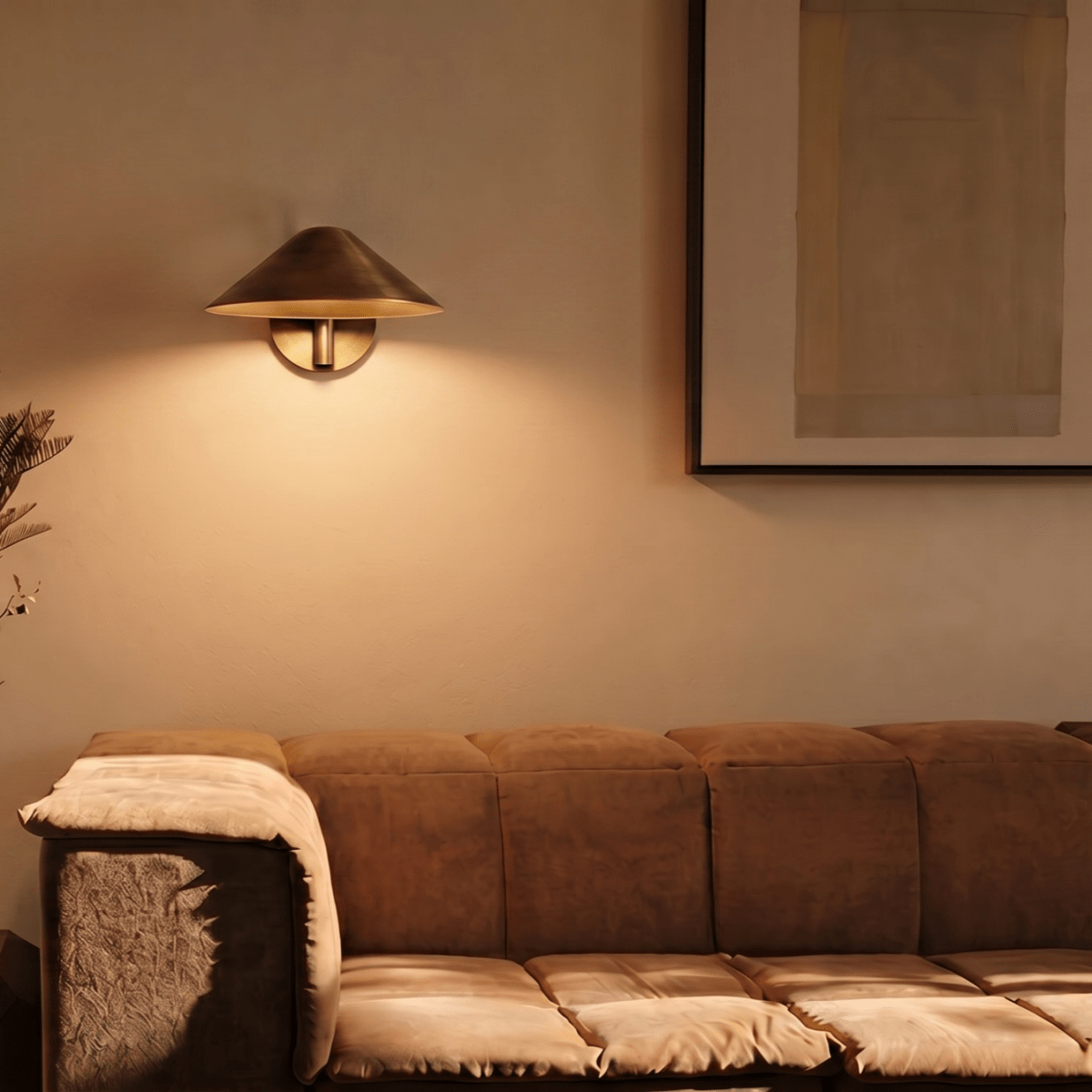 Clérachic vintage brass cone-shade wall sconce lit above a sofa beside a large framed abstract print.