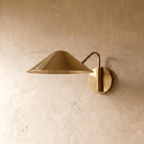 Clérachic cone-shade wall sconce in polished brass, shown from a slightly closer studio angle on a plaster wall.