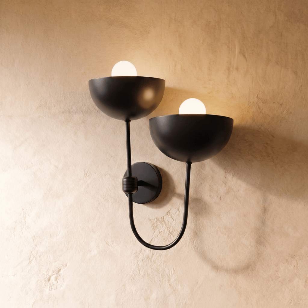 Clérachic wall lamp in matte black, twin dome shades on a looping arm glowing against plaster.