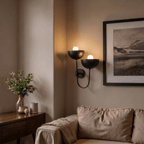 Clérachic wall lamp in matte black beside a framed mountain photograph above a living room sofa.