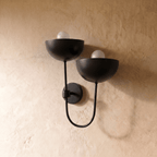 Clérachic wall lamp in matte black shown from another angle, two globe bulbs glowing beneath the domes.
