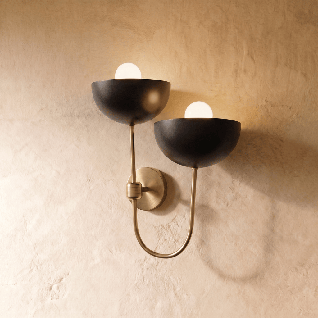 Clérachic wall lamp in brushed brass, twin black dome shades curving from a looping brass arm.
