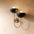Clérachic wall lamp in brushed brass, twin black dome shades curving from a looping brass arm.