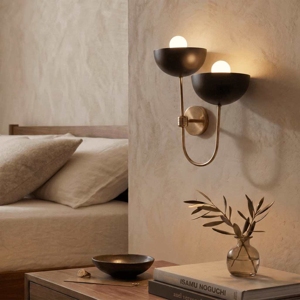 Clérachic wall lamp in vintage brass above a bedside table with stacked design books and a small vase.