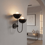 Clérachic wall lamp in matte black mounted by an archway leading into a bright entry hall.