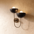 Clérachic wall lamp in vintage brass, twin black dome shades on a looping brass arm against plaster.