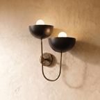 Clérachic wall lamp in vintage brass, twin black dome shades on a looping brass arm against plaster.