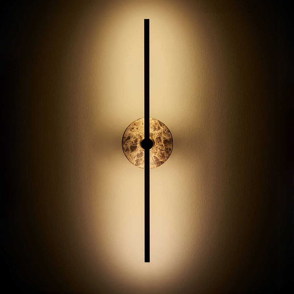 Clérachic wall light illuminated on a dark background, warm light spilling around its brown marbled stone disc.