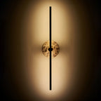 Clérachic wall light illuminated on a dark background, warm light spilling around its brown marbled stone disc.