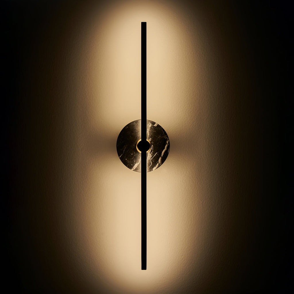 Clérachic wall sconce glowing on a dark background, warm light fanning outward from its brown marbled disc.