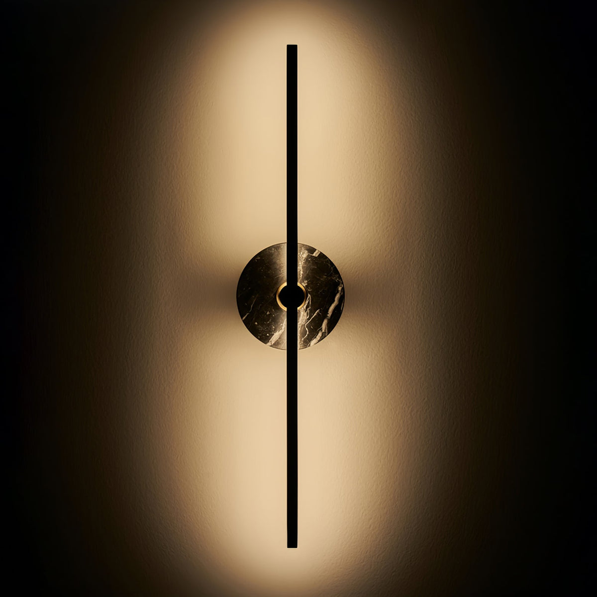 Clérachic wall sconce glowing on a dark background, warm light fanning outward from its brown marbled disc.